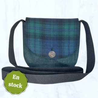 Image carrée sur fond clair. Elle est centrée sur un petit sac arrondi en lin vert foncé, dont le rabat est en tartan vert, bleu foncé et noir. Le rabat du sac est fermé par un bouton rond argenté. Les hanses du sac sont noires. Dans le coin en bas à gauche, il y a une vignette avec noté "En stock".