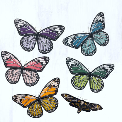 6 papillons en tissus brodés ressortent sur un fond gris clair. 5 d'entre eux ont la même forme et sont dans des coloris vives et variées (tons violets, tons bleus, tons verts, tons roses et tons orangés, au choix). Le 6ème est plus petit, et représente un papillon sphinx tête de mort. Ces papillons sont montés sur des barrettes à cheveux.
