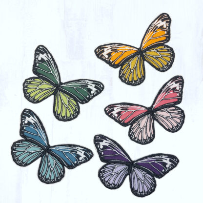5 papillons en tissus brodés ressortent sur un fond gris clair. Ils ont la même forme et sont dans des coloris vives et variées (tons violets, tons bleus, tons verts, tons roses et tons orangés, au choix). Ces papillons sont des patch à thermocoller.