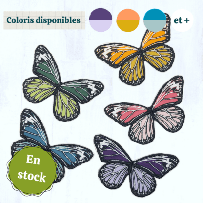 5 papillons en tissus brodés ressortent sur un fond gris clair. Ils ont la même forme et sont dans des coloris vives et variées (tons violets, tons bleus, tons verts, tons roses et tons orangés, au choix). Ces papillons sont des patch à thermocoller. En haut de l'image se trouvent des vignettes indiquant les coloris disponibles, et en bas à gauche se trouve un macaron indiquant "en stock".