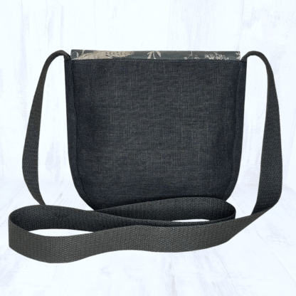 Image carrée sur fond clair. Elle est centrée sur une vue de dos d'un petit sac arrondi en lin noir. Les hanses du sac sont noires.