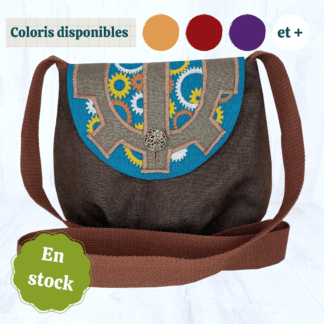 Photo d'un sac en lin marron chocolat. Son rabat de forme arrondie est en lin bleu turquoise sur lequel sont brodés des engrenages argentés, dorés et cuivrés. Par dessus est cousu un gros engrenage en lin marron glacé. Tout en haut de l'image, on peut lire "Coloris disponibles" avec des pastilles colorés juste à côté. Tout en bas, il y a également une pastille indiquant "En stock".